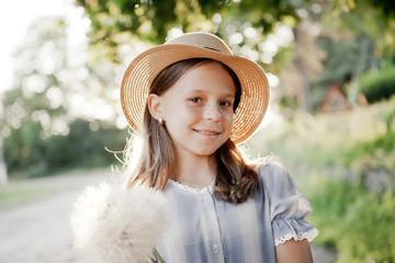 Girl in a hat in the sunset with a large bouquet of dandelions. Playing with a dandelion petal