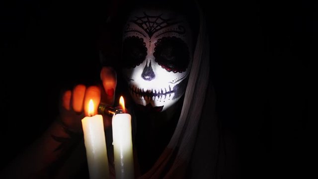 Halloween mask. Girl with candles in the flame of light. Mexican day of the dead. Portrait of a young woman with scary makeup for Halloween on a dark background. 4K