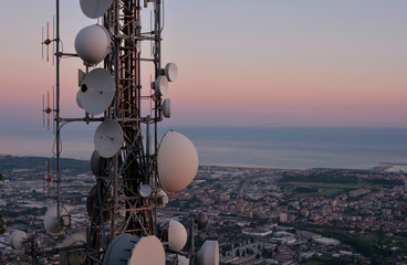 Telecommunications tower, antenna and satellite dish and aerial view of the city as background,...