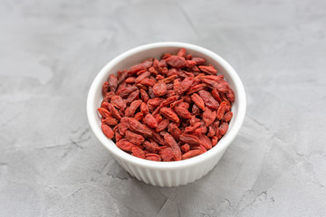Dried goji berries in a porcelain bowl on a gray background