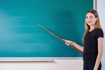 Young attractive student at the school board. She rejoices at the beginning of the school year and holds a pointer in her hands. Back to school. Copy space