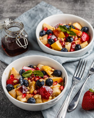 Fruit salad with apples, bananas, strawberries, blueberries, pomegranate seeds, pine nuts, yogurt and honey