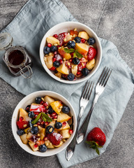 Fruit salad with apples, bananas, strawberries, blueberries, pomegranate seeds, pine nuts, yogurt and honey