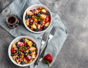Fruit salad with apples, bananas, strawberries, blueberries, pomegranate seeds, pine nuts, yogurt and honey