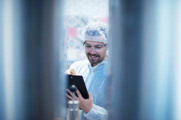 Professional technologist in white protective suit checking production and writing results in food factory.