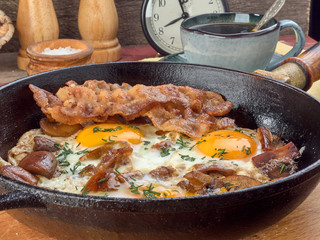 Fried eggs with mushrooms and bacon.Fried corn.On a black iron pan.On wooden background
