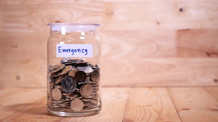 Woman drop coin in the bottle glass to save money for travel on wood background (Thai currency, THB coin)