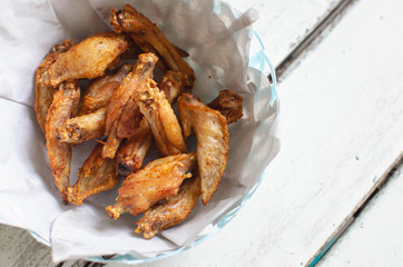 Fried chicken wings with fish sauce. Put on absorb oil paper in bowl. This dish is a popular menu in Thai restaurants. Food on white wooden table with copy space. Look tasty and delicious.