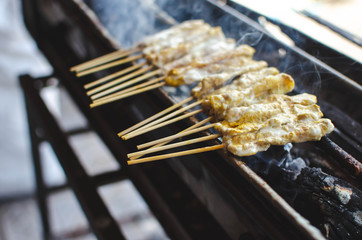 Satay on hot charcoal grill. There is smoke when grilling. Thailand street food. Very popular and...