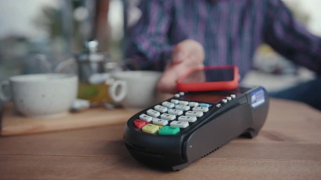 NFC technology concept. Close-up view oung man customer doing payment with contactless paypass technology on mobile phone. People in the cafe. Comfort transaction.