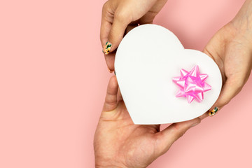 Top view of male and female hands holding shape heart  gift box with pink bow on yellow background Flat lay. Present for birthday, valentine day, Christmas, New Year. 