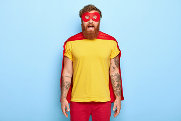 Heroic man with stupefied scared expression, stares through red mask, wears yellow t shirt and...