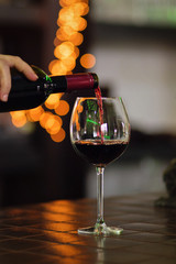 Obraz premium Red wine pouring into wine glass. Shallow depth of field. Bokeh. Warm toning. Space for text. Concept alcoholic drinks. 