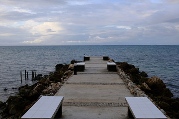 Pier with benches surrounded by water with cloudy sky