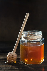 A jar of honey and a spoon for honey on a wooden table. Healthy food, natural products. Dark photo. Copy space, side view.