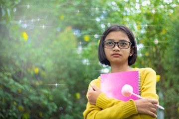 Asian young girl hold pink book and wear glasses at the garden.