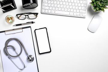 White doctors desk with stethoscope, blank screen smart phone, pen, keyboard and cup of coffee.Top view with copy space