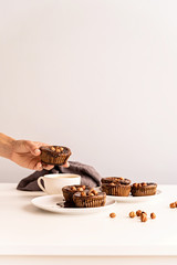 Homemade chocolate cupcakes with glazing, walnuts and a cup of coffee on white table front view