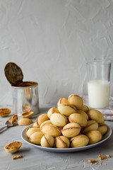 Homemade cookies in the form of nuts with boiled condensed milk and fresh milk in the background. Side view, copy space, vertical orientation.