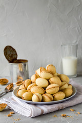 Homemade cookies in the form of nuts with boiled condensed milk and fresh milk in the background. Side view, copy space, vertical orientation.
