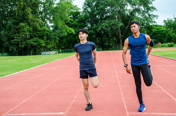 Obraz premium Training teammates. Two male athletes is warming-up,Two runners standing on the racetrack at the stadium stretching their legs before running