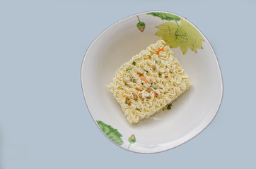On the plane of the table is a plate with a dry briquette of pasta for quick preparation of meals, close-up.