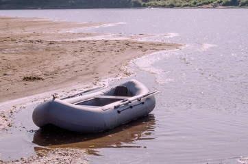 On the river surface on a calm summer day at the sandy shore moored inflatable double boat designed...