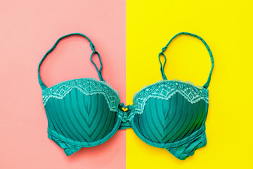 Neatly laid green bra on pink and yellow background. Flat lay. - obrazy, fototapety, plakaty