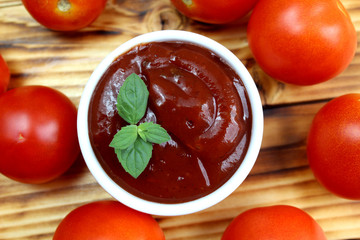 Ketchup in a cup and fresh tomatoes lie on a wooden table close-up