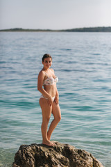 Fototapeta na wymiar Sexy woman sit on stone in bikini. Background of sea