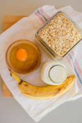 Bowl with egg and banana with cereals in glass jar with milk bottle on table, ingredients for cocking pancakes concept