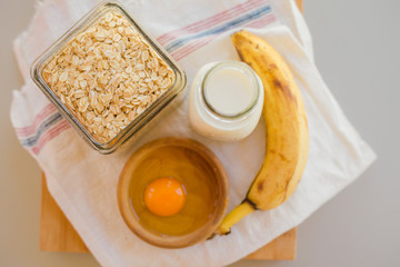 Bowl with egg and banana with cereals in glass jar with milk bottle on table, ingredients for...