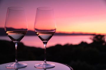 Two glasses of white wine with pink sunset and sea in the background
