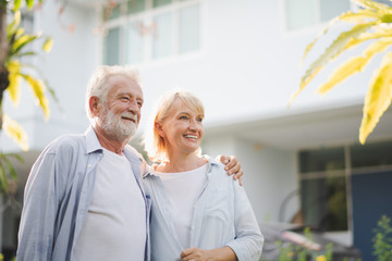 Seniors European couple man and woman are standing at outdoor green garden in retirement home. Retired couple are smiling felling happy and looking out of camera.