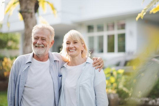 Seniors European couple man and woman are standing at outdoor green garden in retirement home. Retired couple are smiling felling happy and looking out of camera.