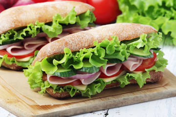 Two sandwiches with fresh vegetables, ham and cheese in ciabatta bread