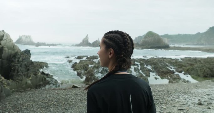 Young woman walks towards the Atlantic ocean in northern Spain on an epic and rocky beach during low tide. Gueirua Beach in northern Spain.