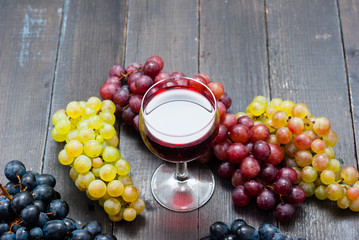glass of red wine and grapes on black wooden table background