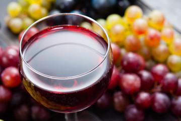 glass of red wine and grapes on black wooden table background