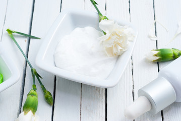 cosmetic cream and white carnation flowers on bright wooden table