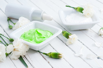 cosmetic creams, perfume in pipette and white flowers on bright wooden