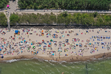 Drone aerial top down view on sunny beach with sunbathers with windbreaks and towels at sea in touristic city