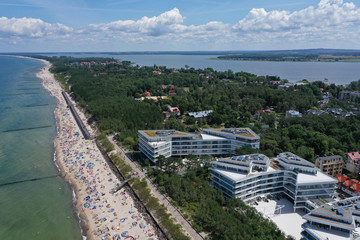 Drone aerial perspective view on sunny beach with sunbathers with windbreaks and towels at sea in touristic city