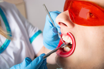 Dentistry. Examination of teeth with the help of a dental mirror close-up. A young man is a patient with an open mouth and Protective goggles.