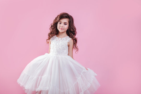 portrait of beautiful little girl in white dress on pink background
