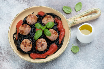 Serving pan with squid-ink spaghetti and roasted pork meatballs, studio shot over beige stone background