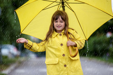 Little girl in raincoat walking with umbrella 