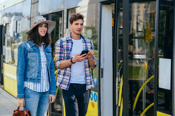 Stylish couple of travelers with backpacks entering into tram at outdoor tram stop.