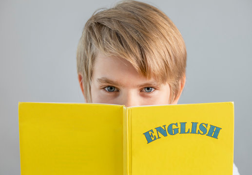Handsome preteen schoolboy holding yellow english book, modern education, foreign languages