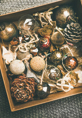 Christmas or New Year preparation. Flat-lay of various vintage Christmas tree decoration toys, balls and pine cones in wooden box over grey knitted blanket background, top view. Festive holiday mood